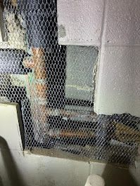 Wire mesh over a stairwell with exposed pipes and a white wall in an industrial interior