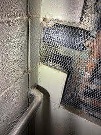 Dim hallway corner with cinder block wall, handrail, and a mesh-covered window or opening.
