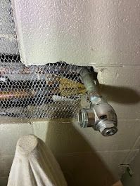 Close-up of a metal pipe and valve protruding from a wall with damaged mesh insulation.