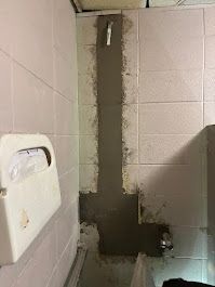 Restroom wall with a vertical dark repair patch beside a white hand dryer.