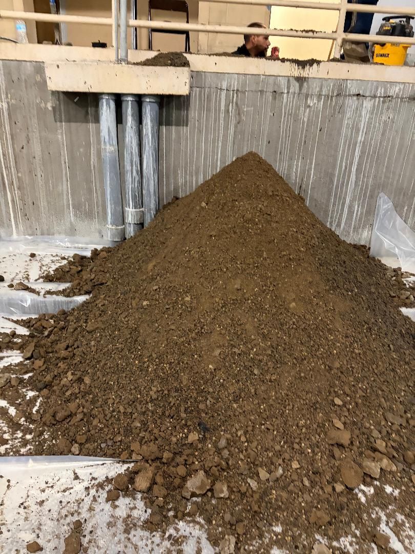 Large mound of dirt or gravel piled in an industrial concrete pit beneath a beam.