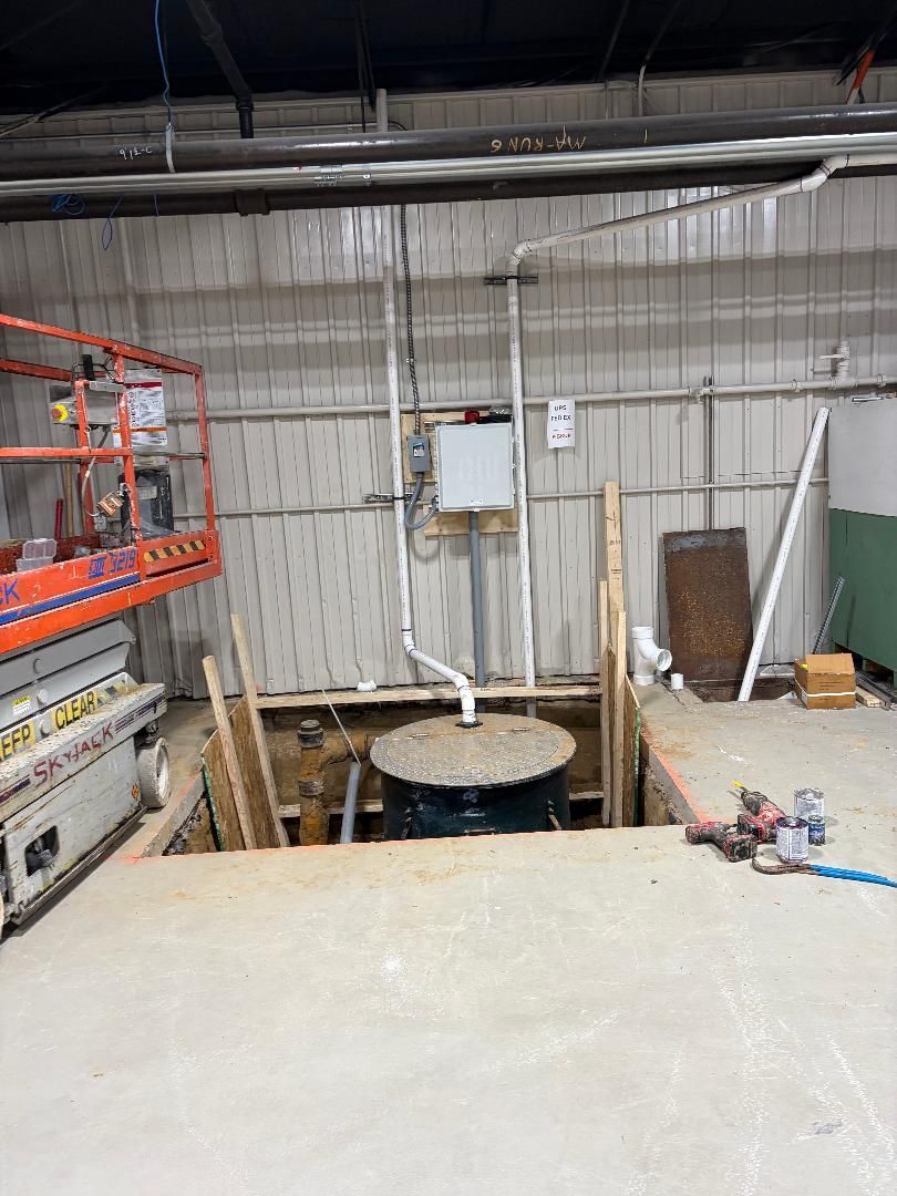 Industrial workspace with shelves, open floor pit, and wall-mounted equipment in a concrete room