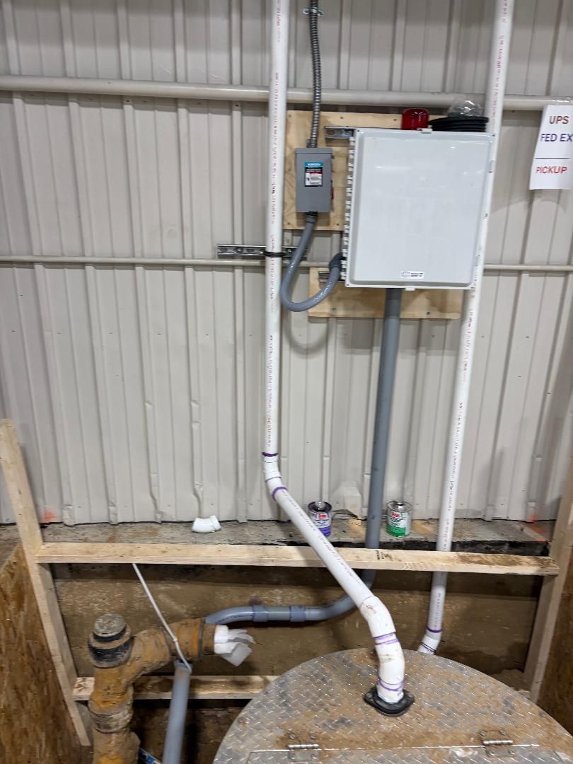Basement utility area with electrical box, pipes, and an access opening in the floor.