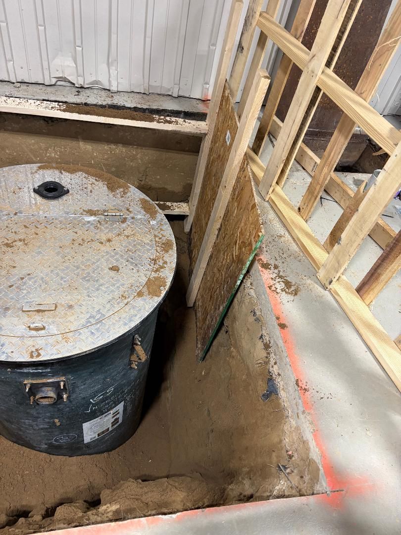 Construction site corner with a large black tank and wooden framing beside a dirt trench.