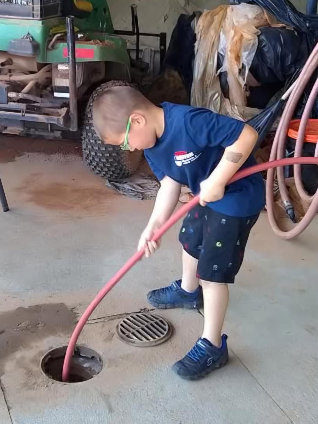 Boy using a red hose to clean a floor drain in a garage.