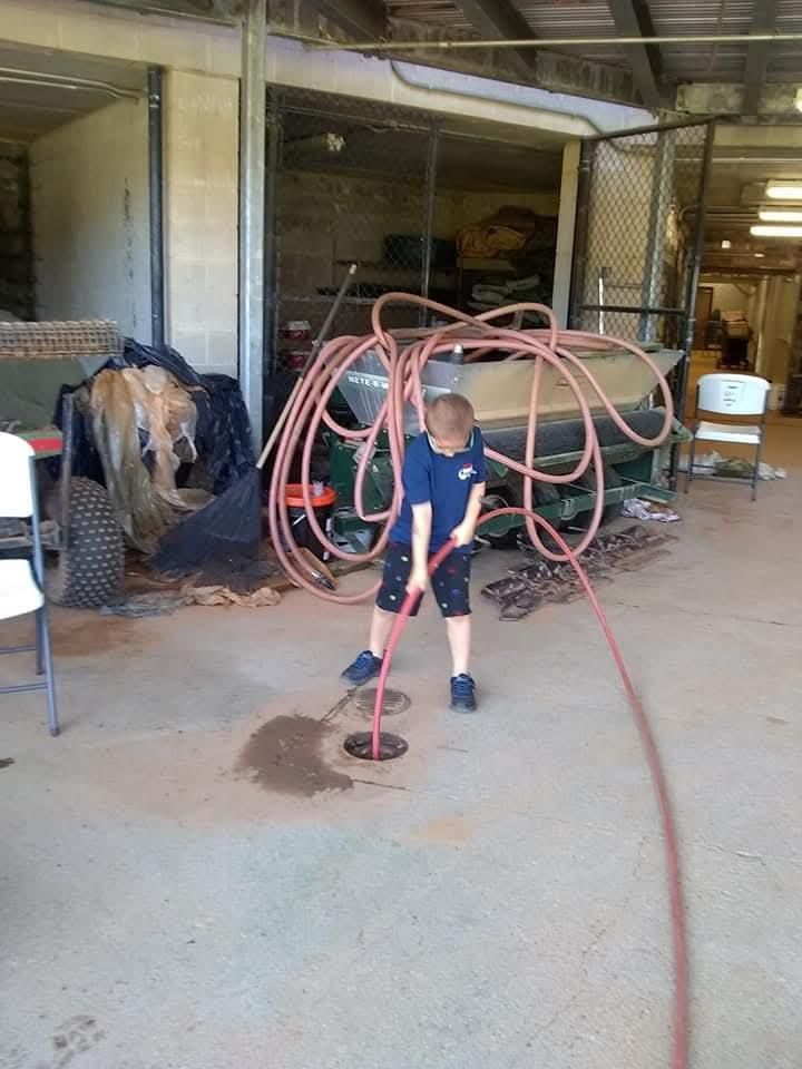 Child holding a hose in a garage, with coiled red hoses and cleaning equipment in the background