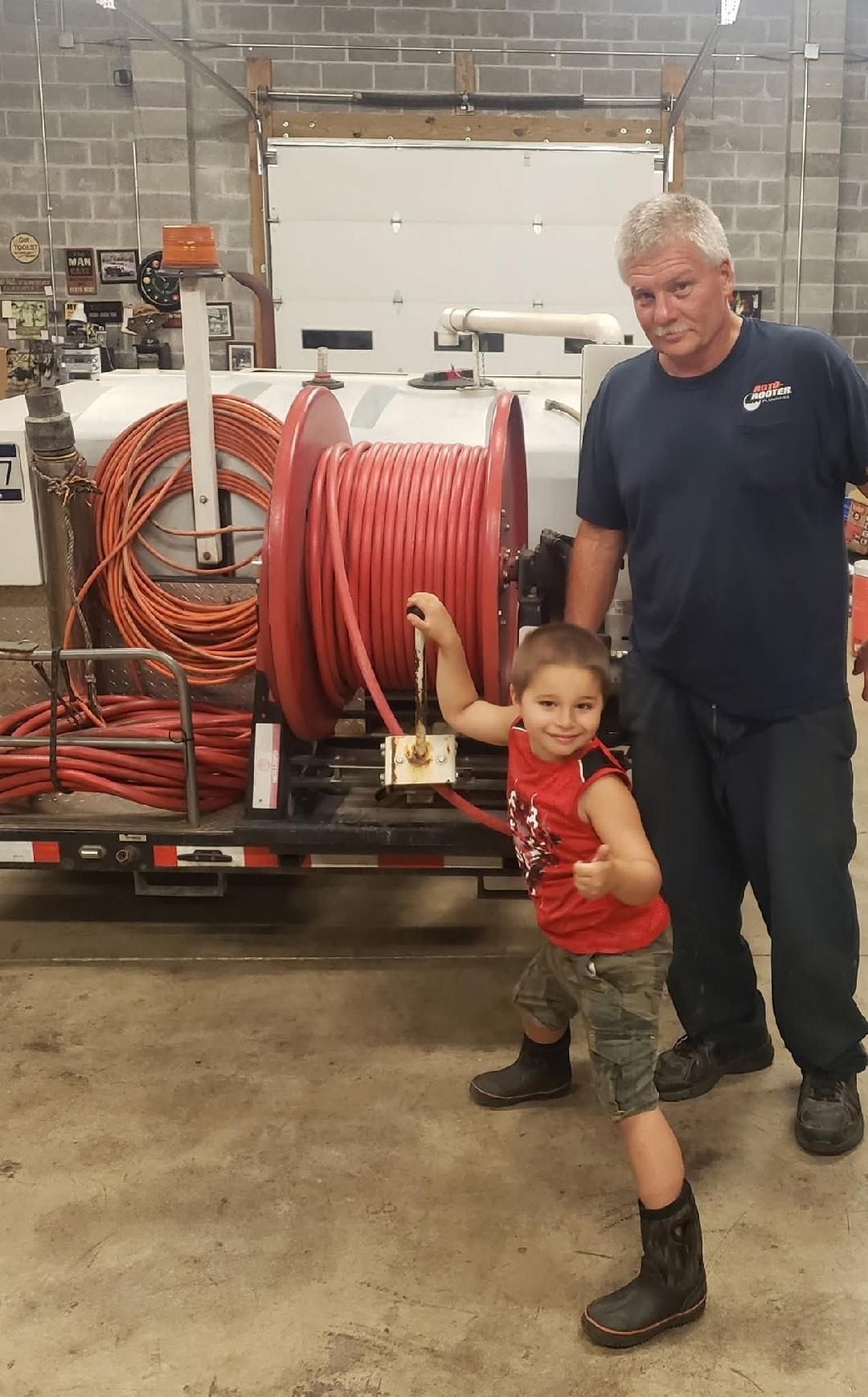 Man and child standing by a truck loaded with coiled red hoses in a workshop