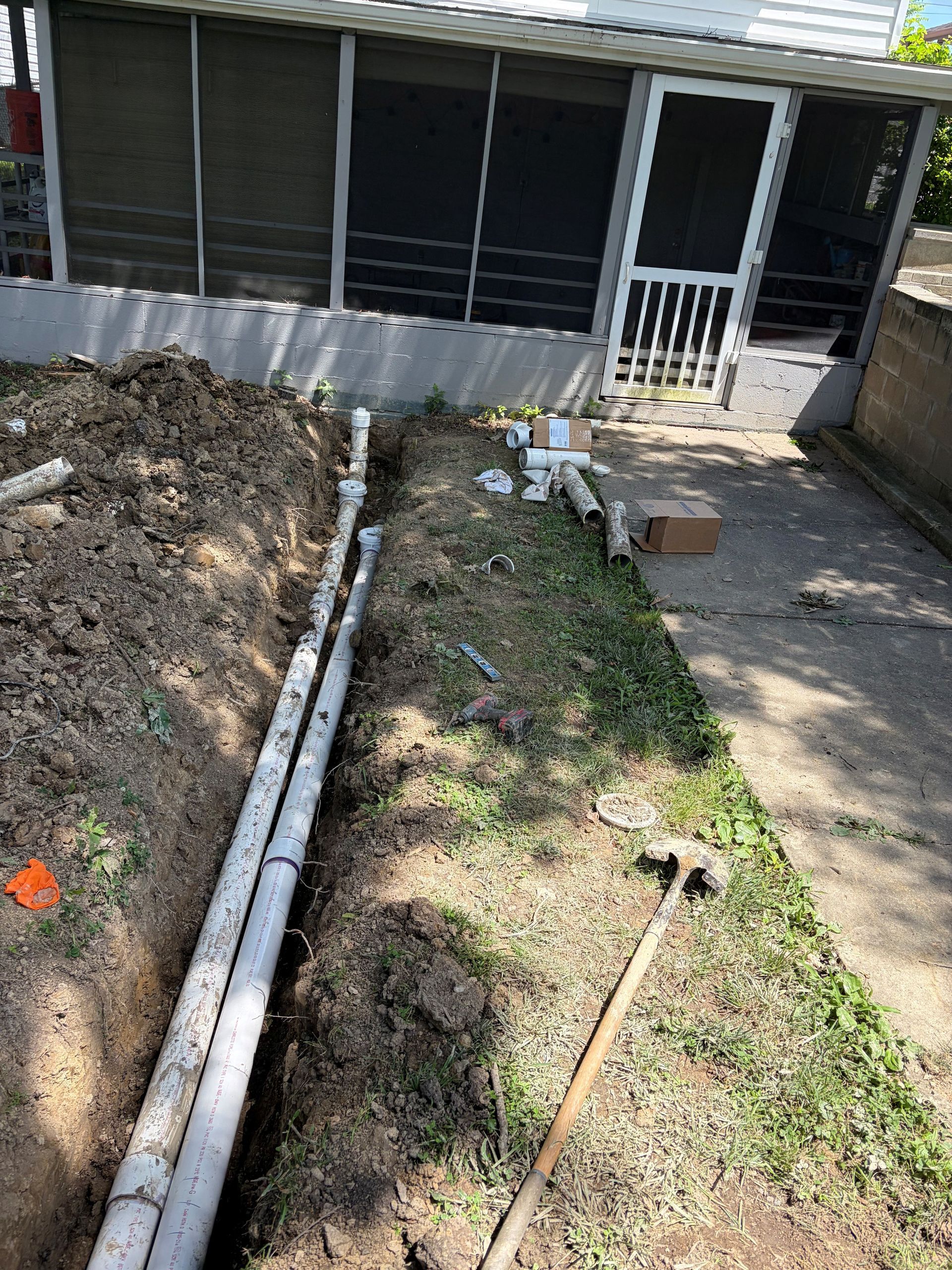 Backyard with dirt pile, long pipes, grass strip, and a house porch in the background