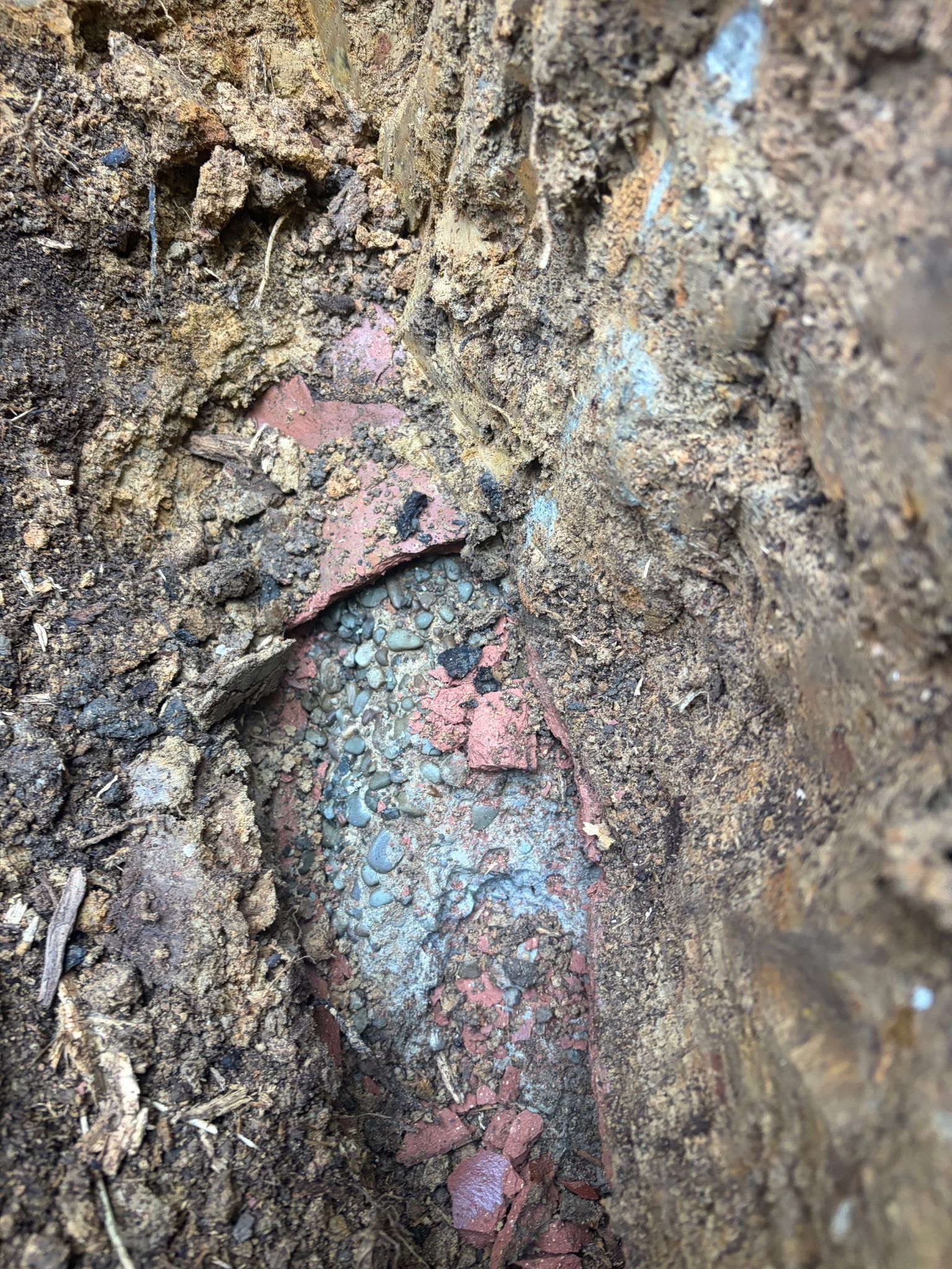 Close-up of a rusty, corroded metal object partially embedded in dirt and rock.
