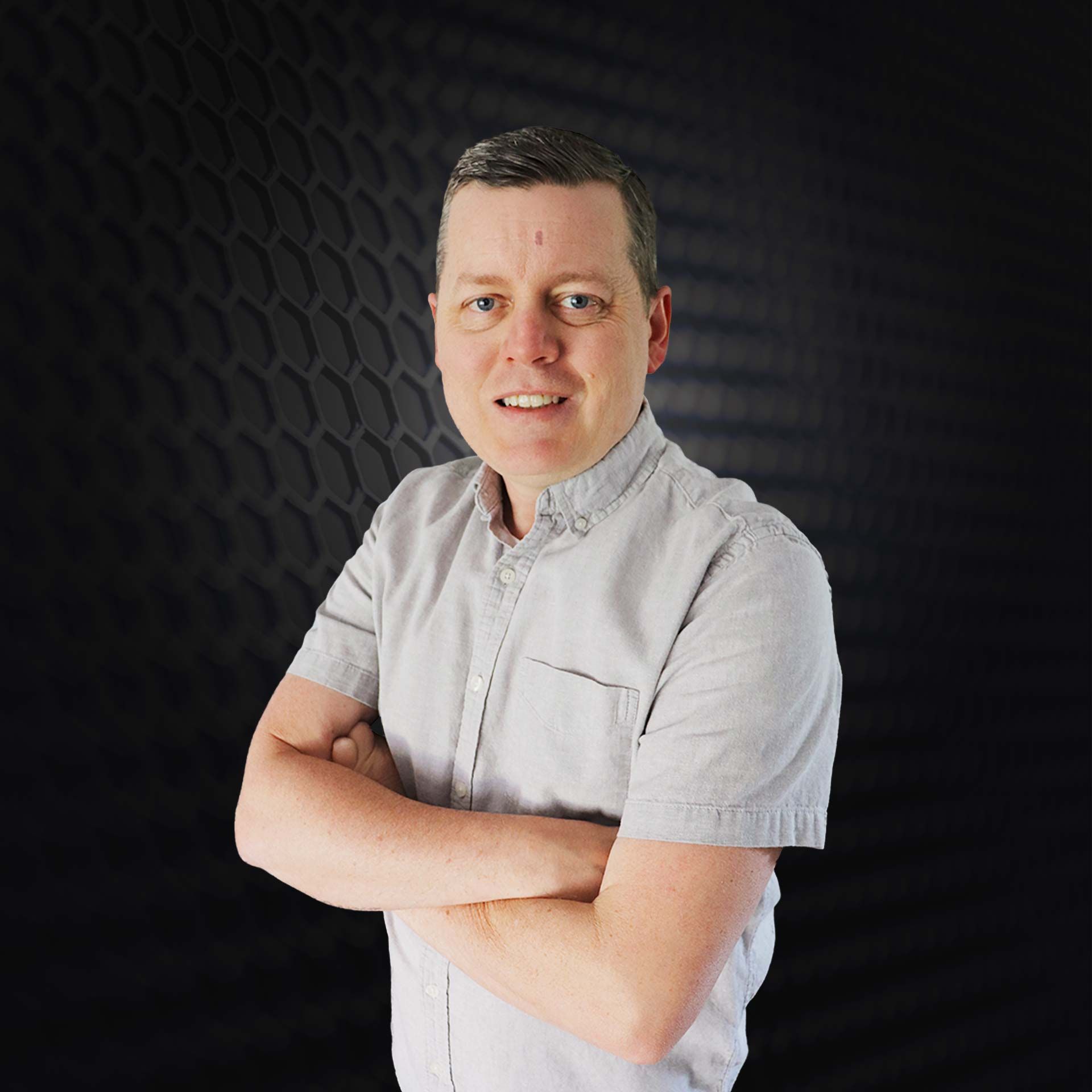 Person standing with arms crossed against a dark textured background, wearing a light gray shirt.