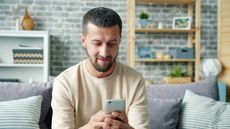 Man sitting on a couch and looking at his phone in a bright living room.