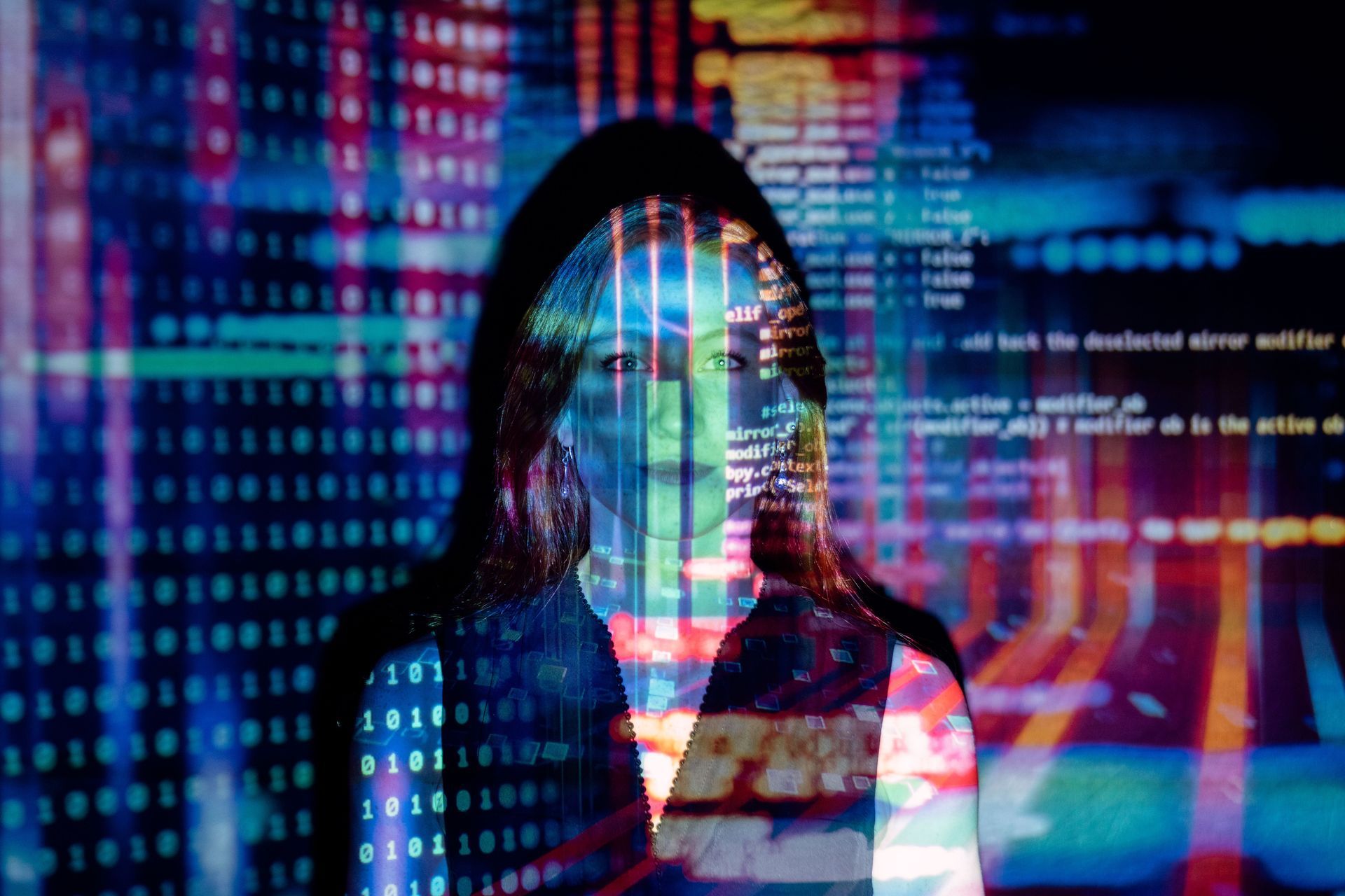 Hooded person overlaid with colorful code and data streams on a digital screen background