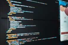 Person coding at a desk with dual monitors in a bright office