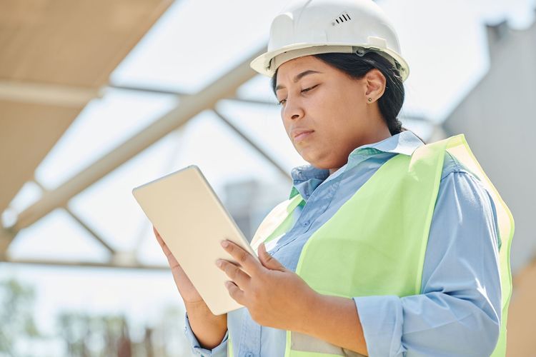 Construction worker in hard hat reviewing plans on a tablet at a job site