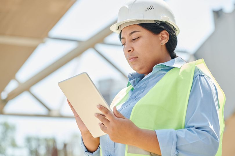 Construction worker in hard hat reviewing plans on a tablet at a job site
