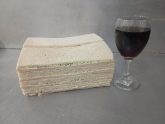 Pila de sándwiches y una copa de vino tinto en un mostrador.