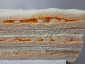 Sándwich cortado por la mitad, apilado. Capas de jamón, ensalada de huevo y pan.