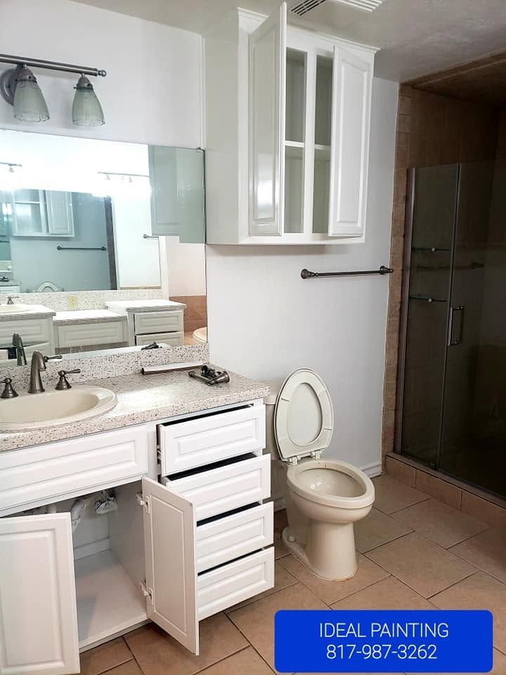 White bathroom vanity with mirror, open cabinet, toilet, and shower stall with tiled floor