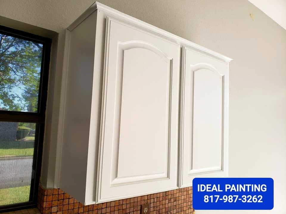 White kitchen cabinet doors being painted on a wall with a small "Ideal Painting" label in the corner