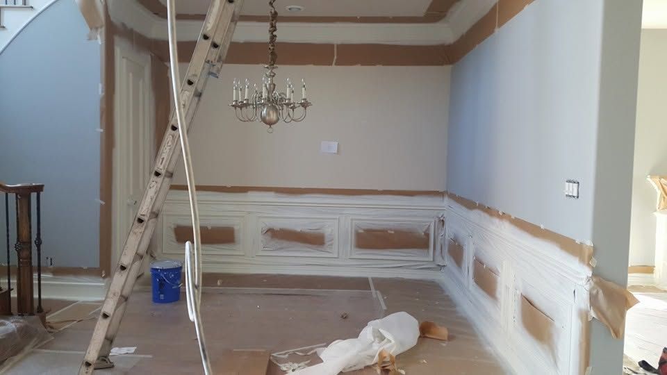 Empty dining room under renovation with ladder, chandelier, and paint prep on walls