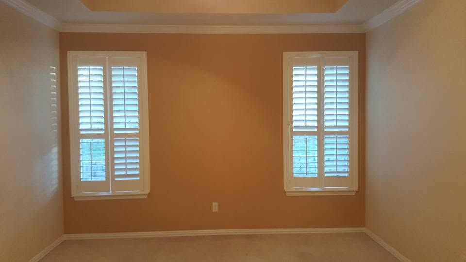 Empty beige room with two windows and white shutters