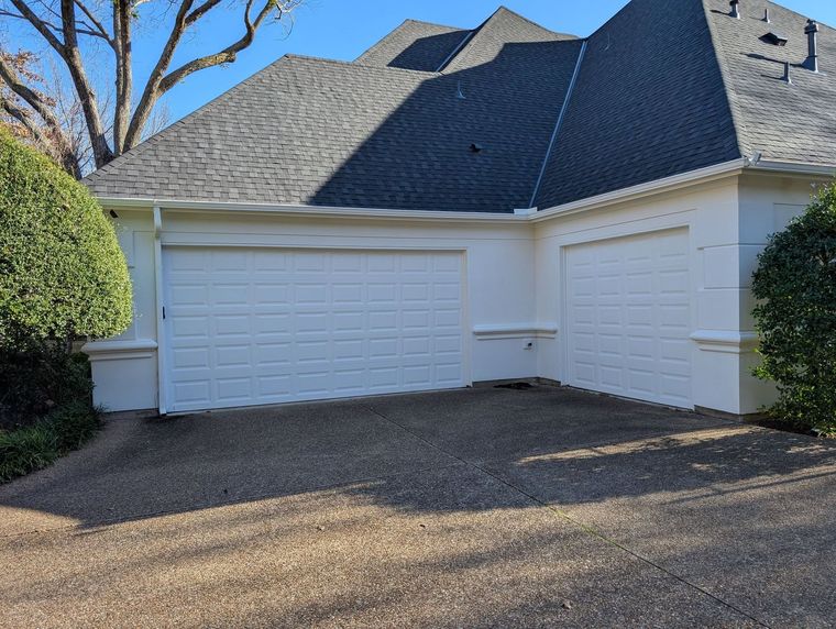 White double garage doors on a light-colored house with a gray shingle roof and gravel driveway