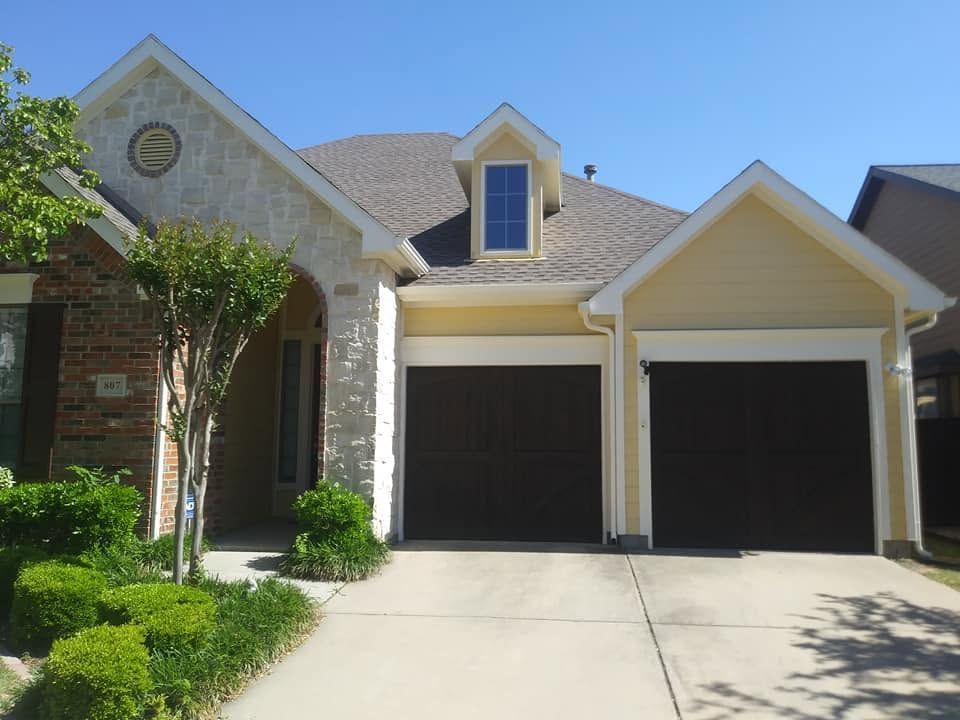 Suburban house with two-car garage, arched entryway, and a sunny driveway.