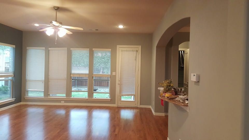 Empty living room with hardwood floors, ceiling fan, large windows, and an archway to the right