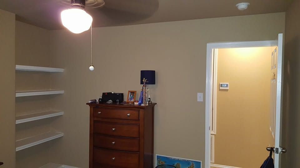 Small bedroom with shelves, dresser, and open doorway to a lit hall.
