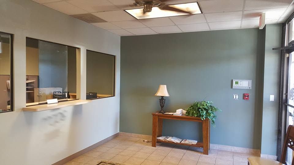Empty office lobby with windows, a small table lamp, and gray-green walls.