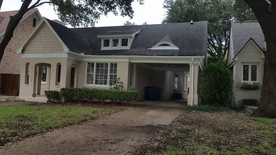 Single-story suburban house with front porch, dormer windows, and a gravel driveway under overcast skies