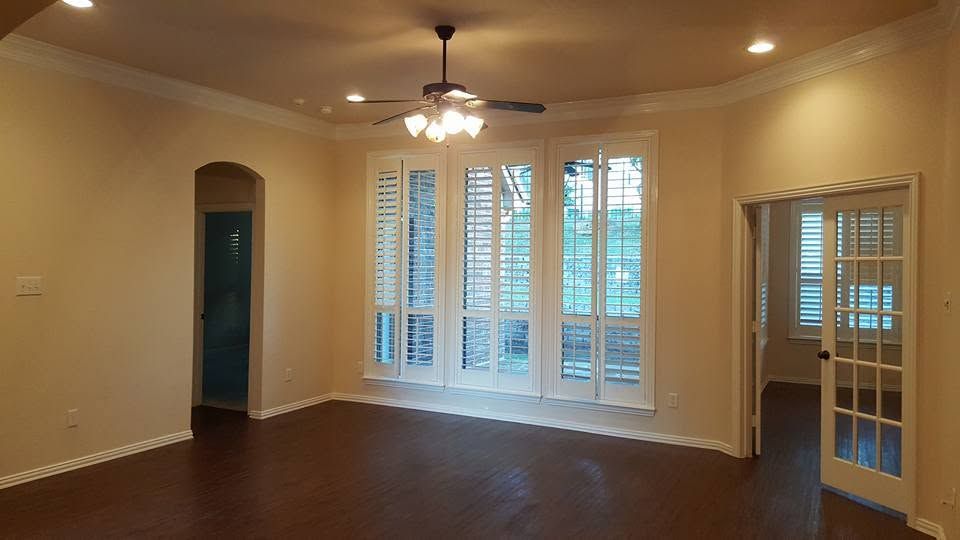 Empty living room with hardwood floors, ceiling fan, and tall windows with shutters.
