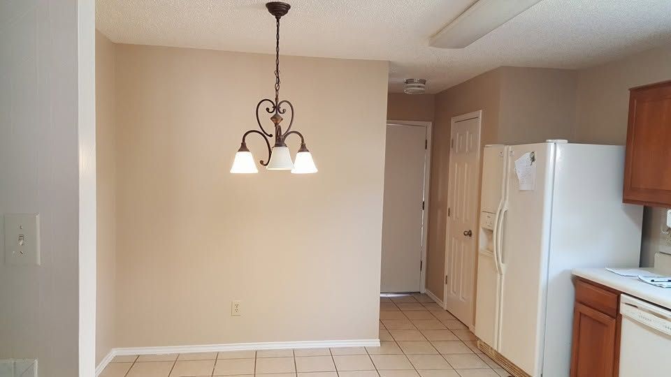 Empty kitchen and dining area with beige walls, tiled floor, hanging light fixture, and white appliances
