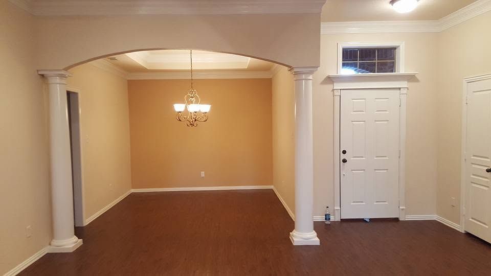 Empty beige dining room with hardwood floors, white columns, and a chandelier above the open archway
