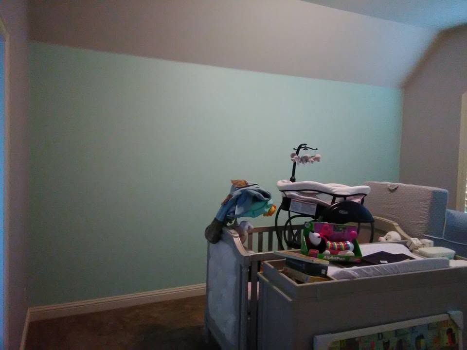 Empty nursery room with mint green walls and a changing table piled with baby items.