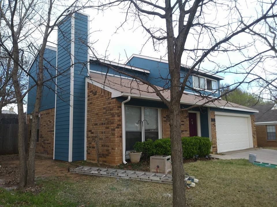 Brick house with blue siding, a white garage, and leafless trees in the front yard