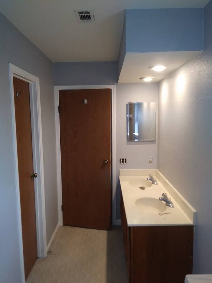 Narrow hallway with two wooden doors and a small bathroom vanity with sink and mirror on the right.