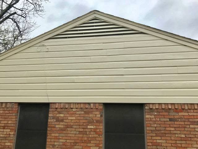 Front gable of a beige house with horizontal siding and brick walls below