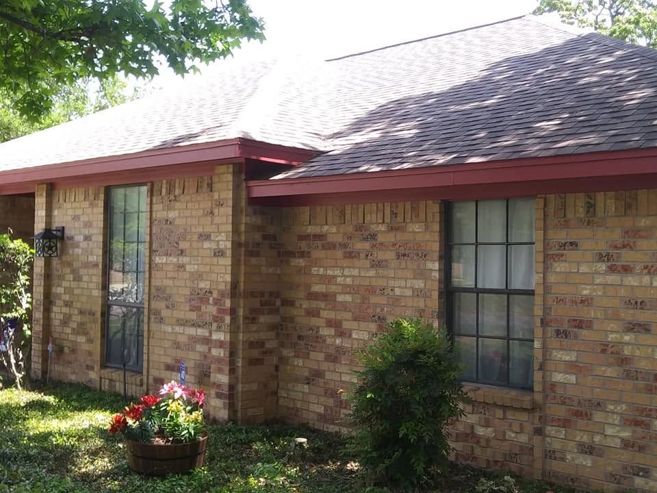 Brick house exterior with red roof, front windows, and flower bed by the porch
