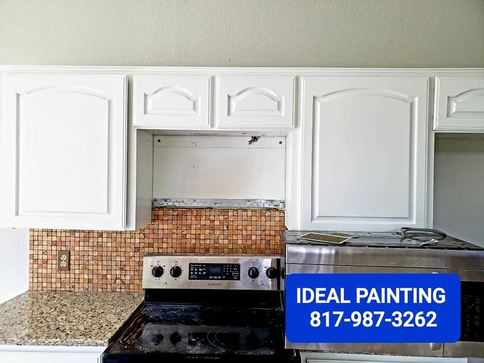 White kitchen cabinets above a stove and granite countertop, with a blue Ideal Painting contact sign.