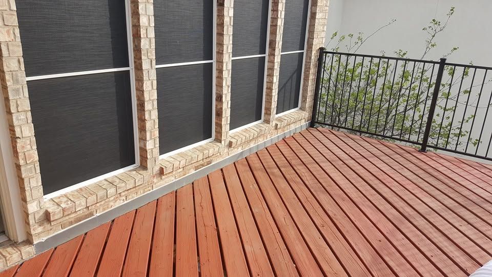 Wooden deck corner beside a house wall with large windows and a black metal railing