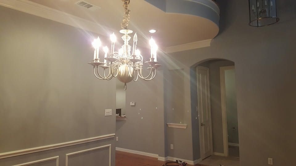 Empty dining room with a lit chandelier, gray walls, white wainscoting, and an open doorway.