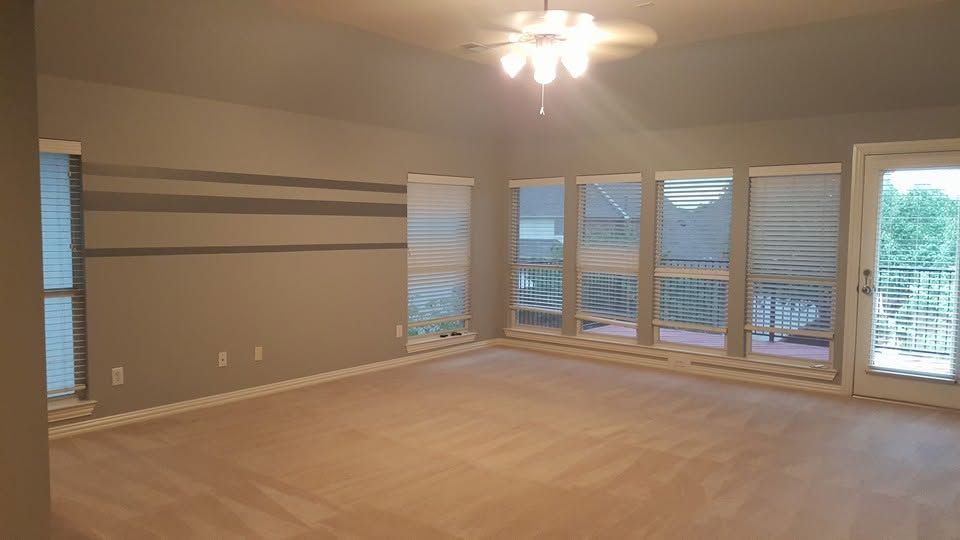 Empty beige living room with ceiling fan, large windows, and sliding glass door overlooking water outside