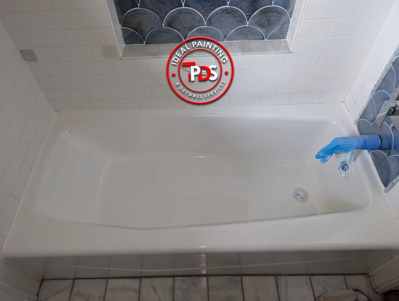 Bathroom bathtub under a window, with a blue glove on the right faucet area.