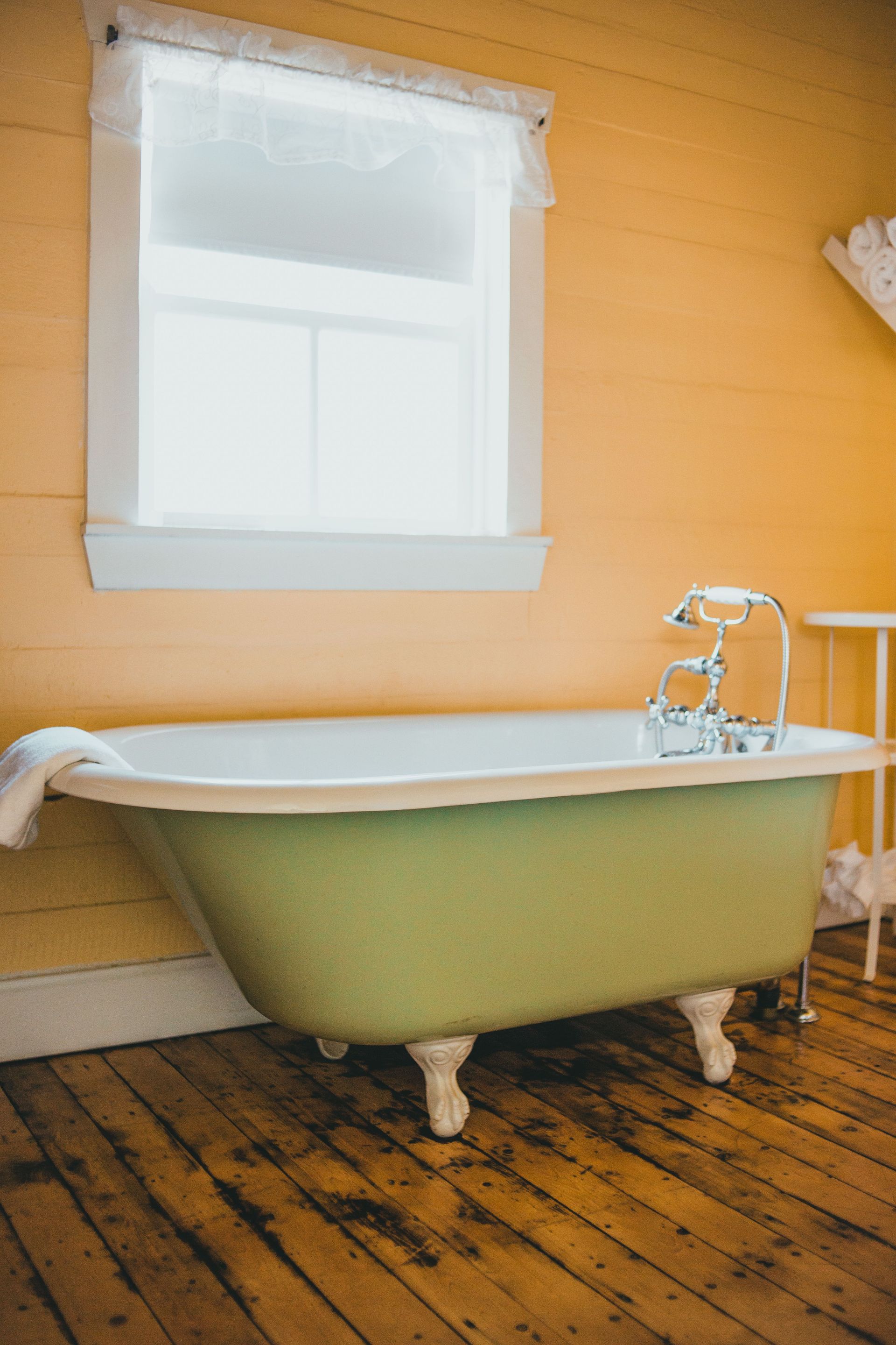 Clawfoot bathtub beneath a frosted window in a small room with yellow walls and worn wooden floor