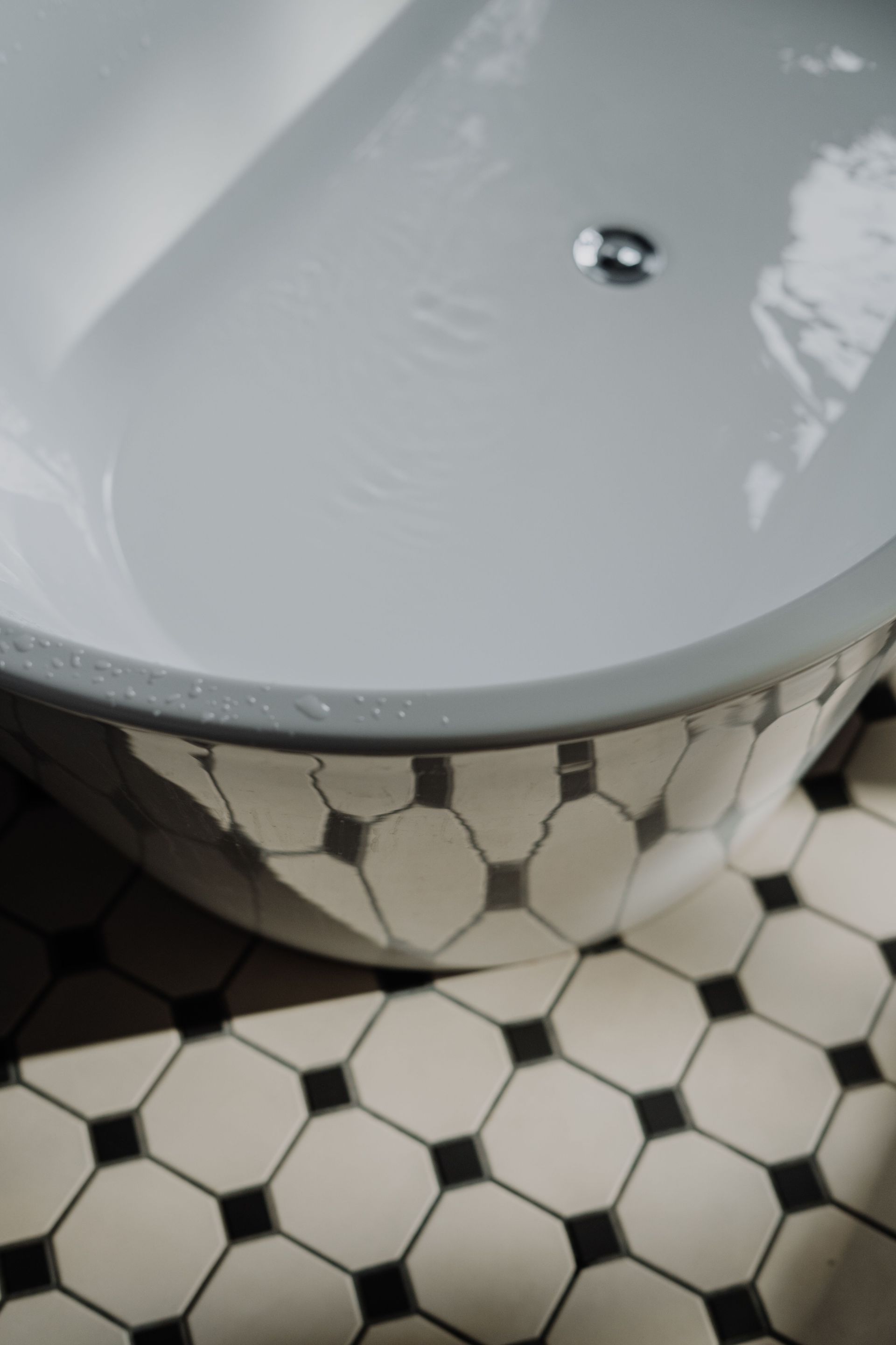 White bathtub with chrome drain above black-and-white hex tile floor