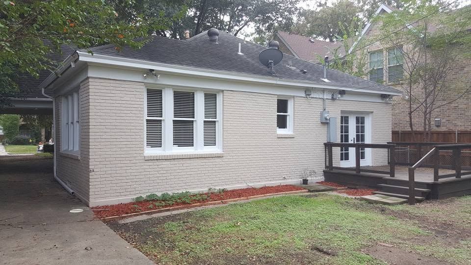 Small light-gray house with white trim, front porch ramp, and a driveway beside it.