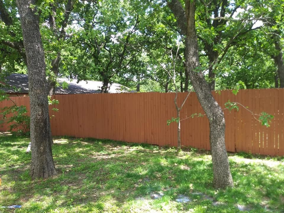 Wooded backyard with green grass, tall trees, and a long orange wooden fence