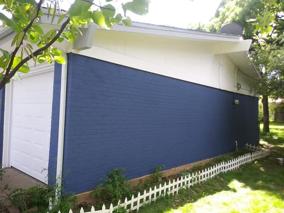Blue house side with white trim and a small white picket fence in a grassy yard.
