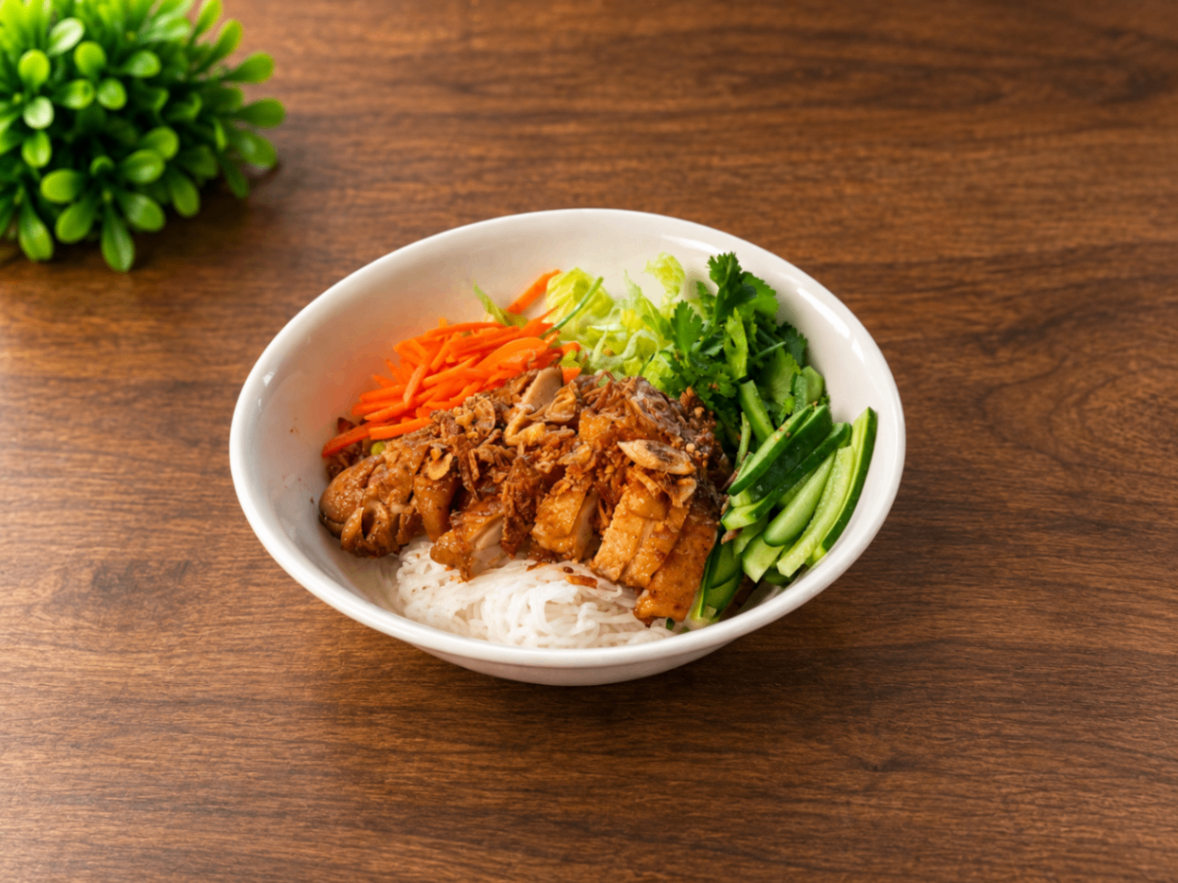 Bowl of rice topped with fried chicken and vegetables on a wooden table